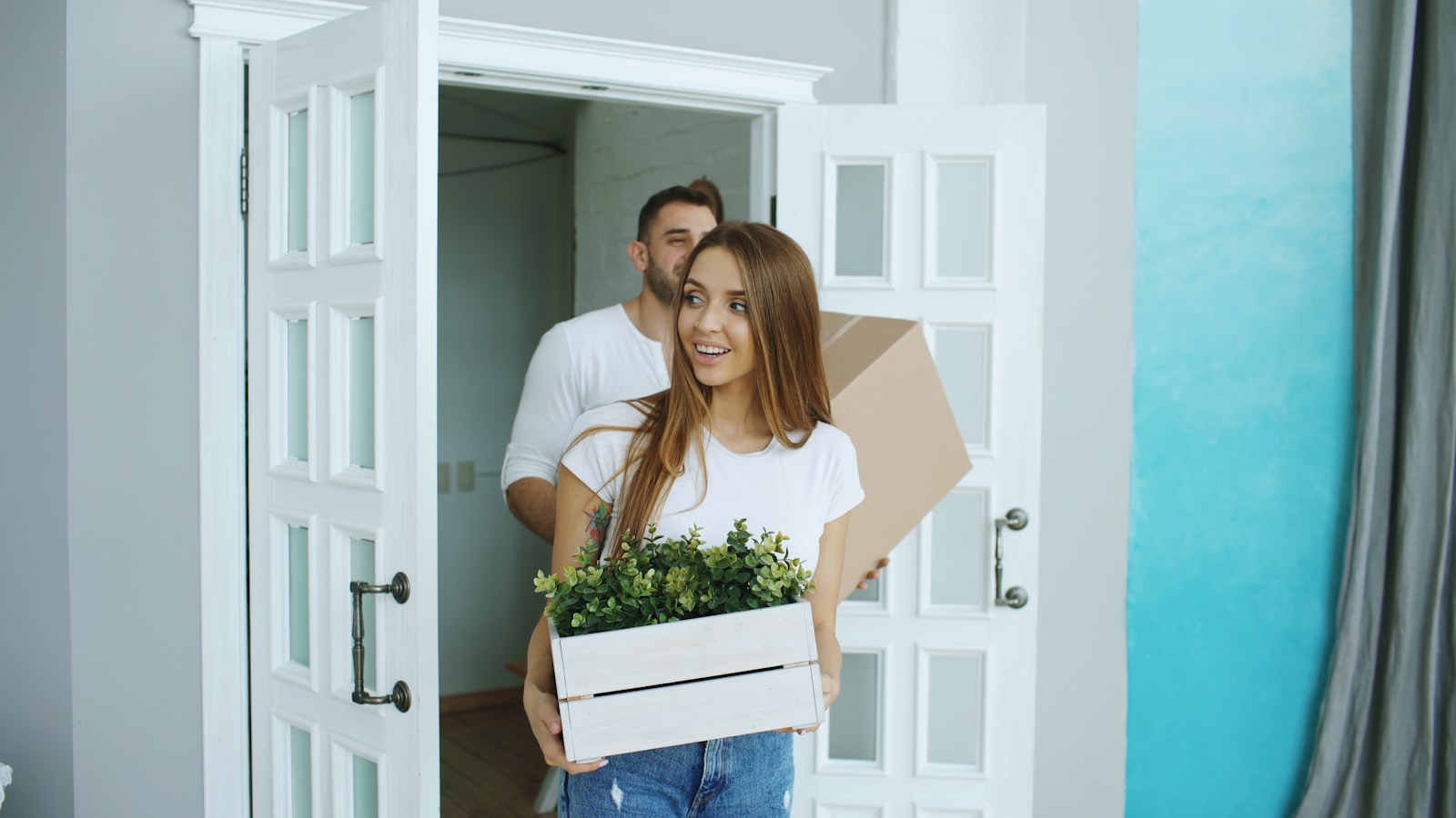 Couple carrying boxes and a plant into their new home